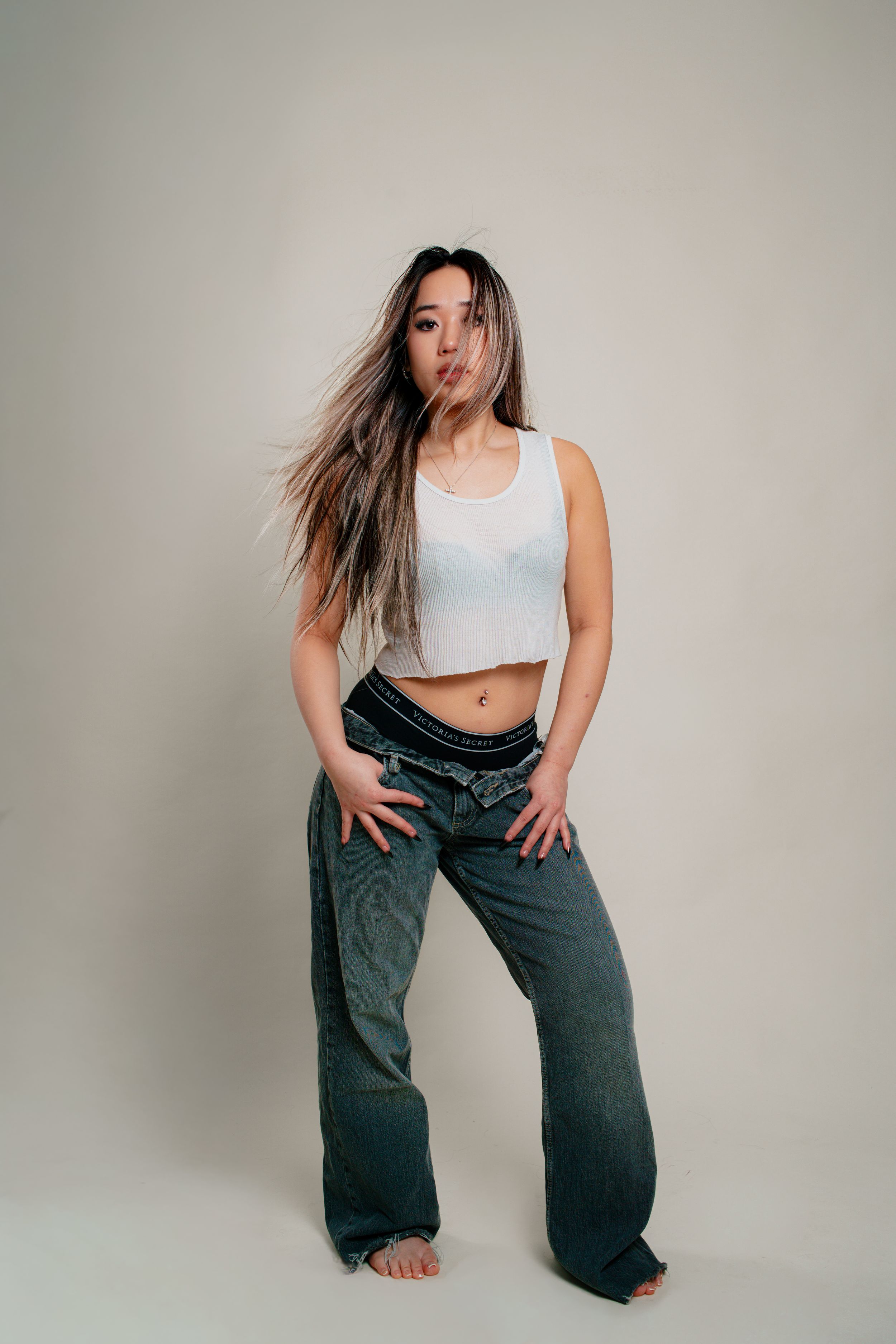 Fashion model in white crop top and dark baggy jeans poses in dynamic sequence against neutral studio backdrop.