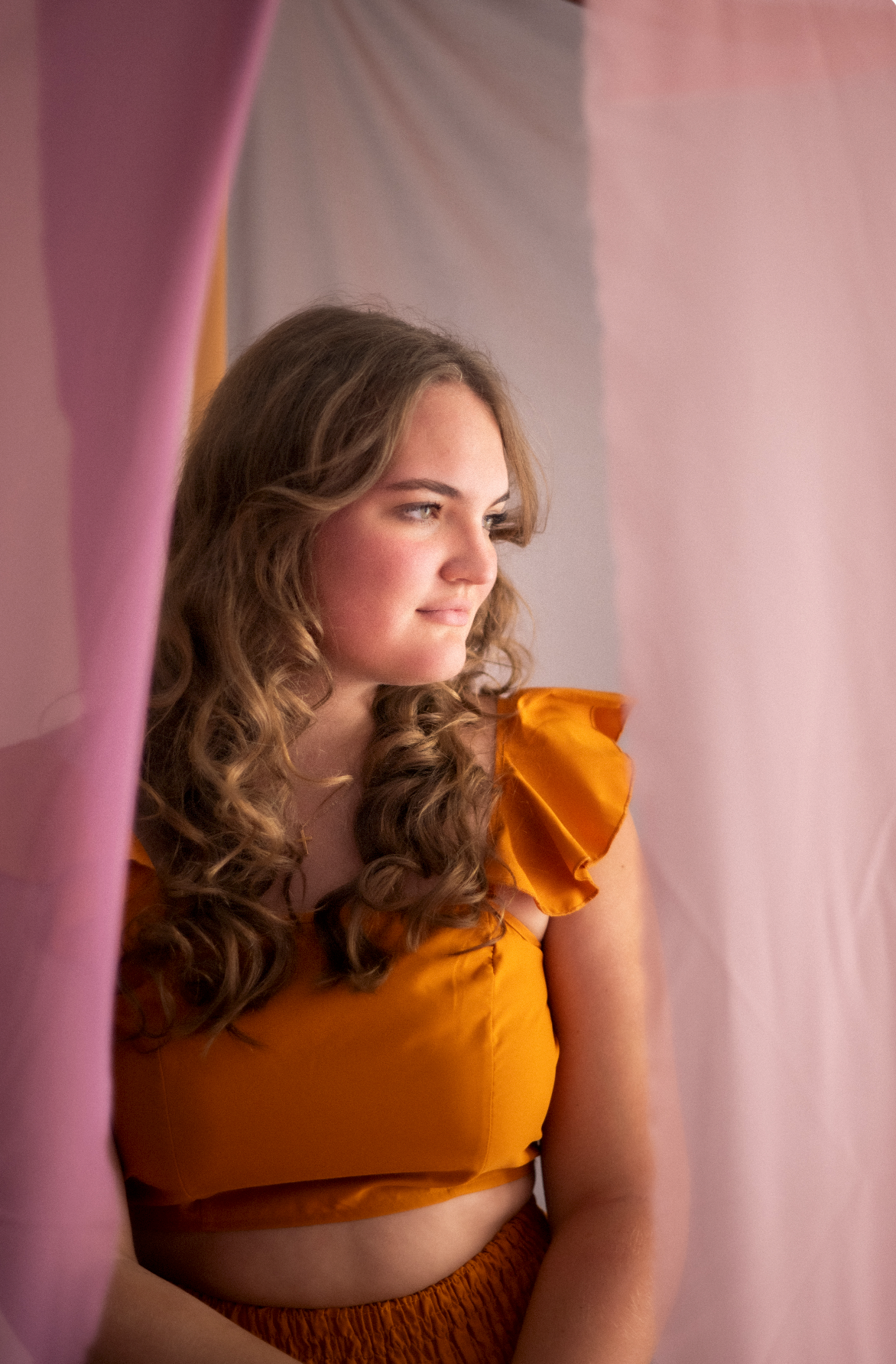 Portrait of a person in an orange ruffled top against a pink backdrop.