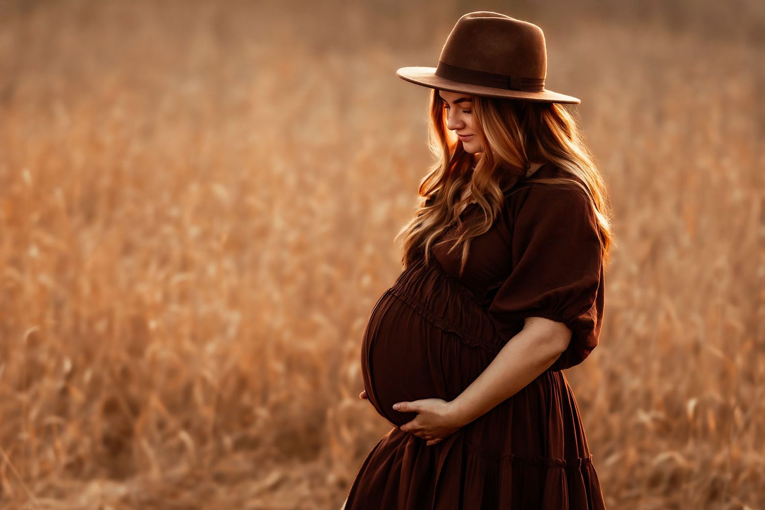 A silhouetted figure in a wide-brimmed hat stands in a golden wheat field at sunset.