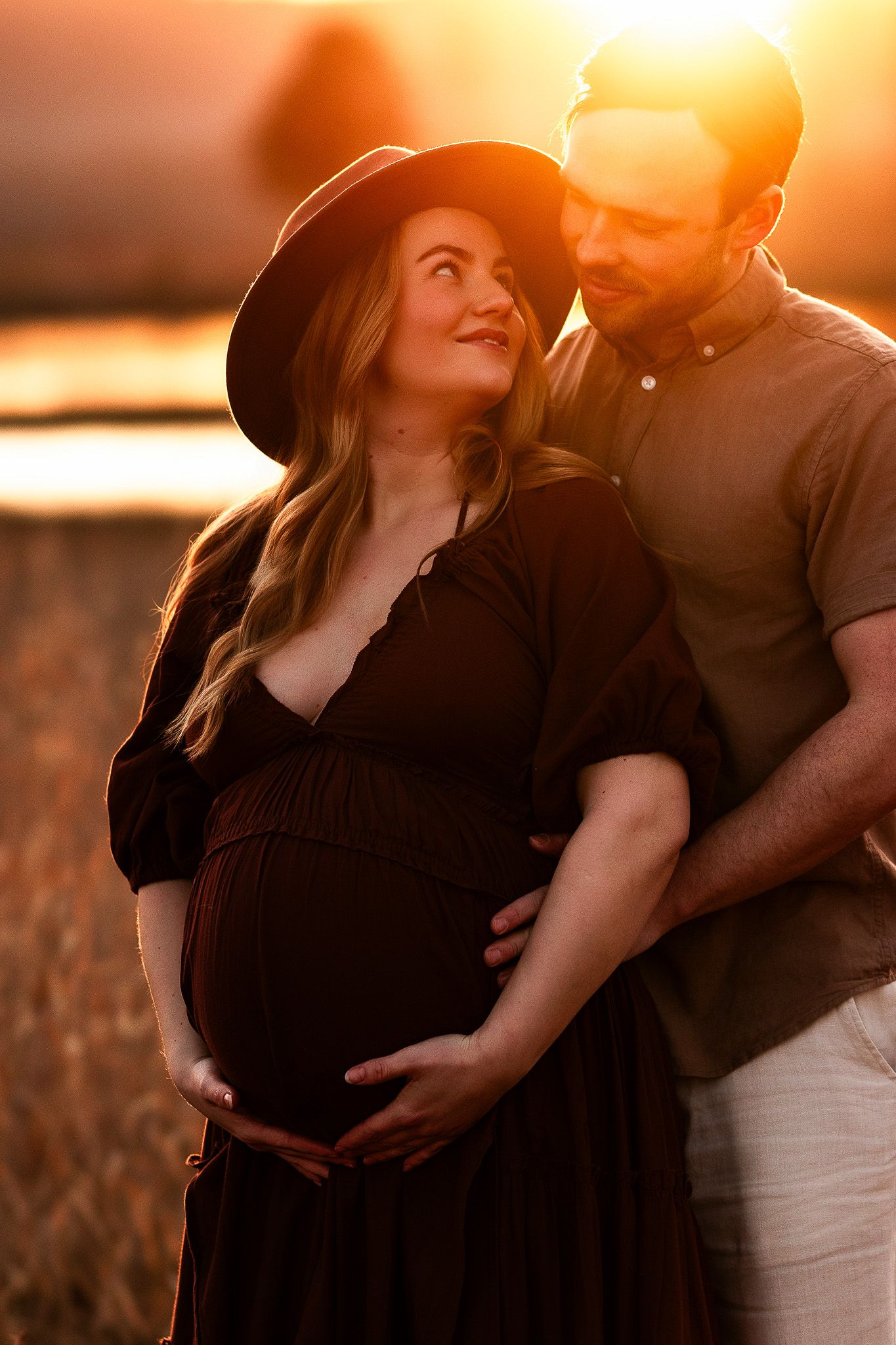 Silhouettes of couple embracing in golden sunset light across field with tall grass and warm orange glow.