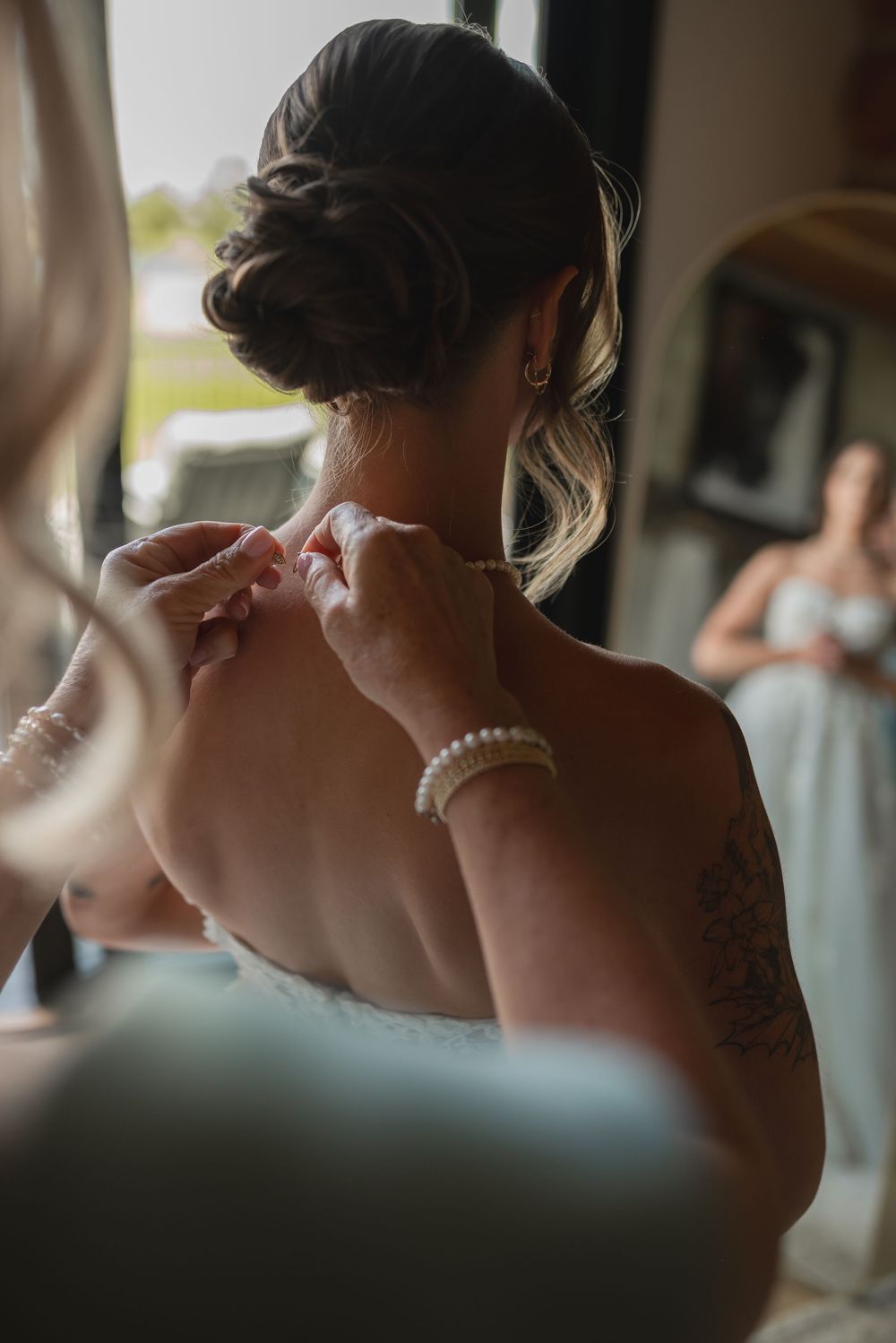 A close-up view of pearl necklace being fastened around a neck during a wedding preparation.