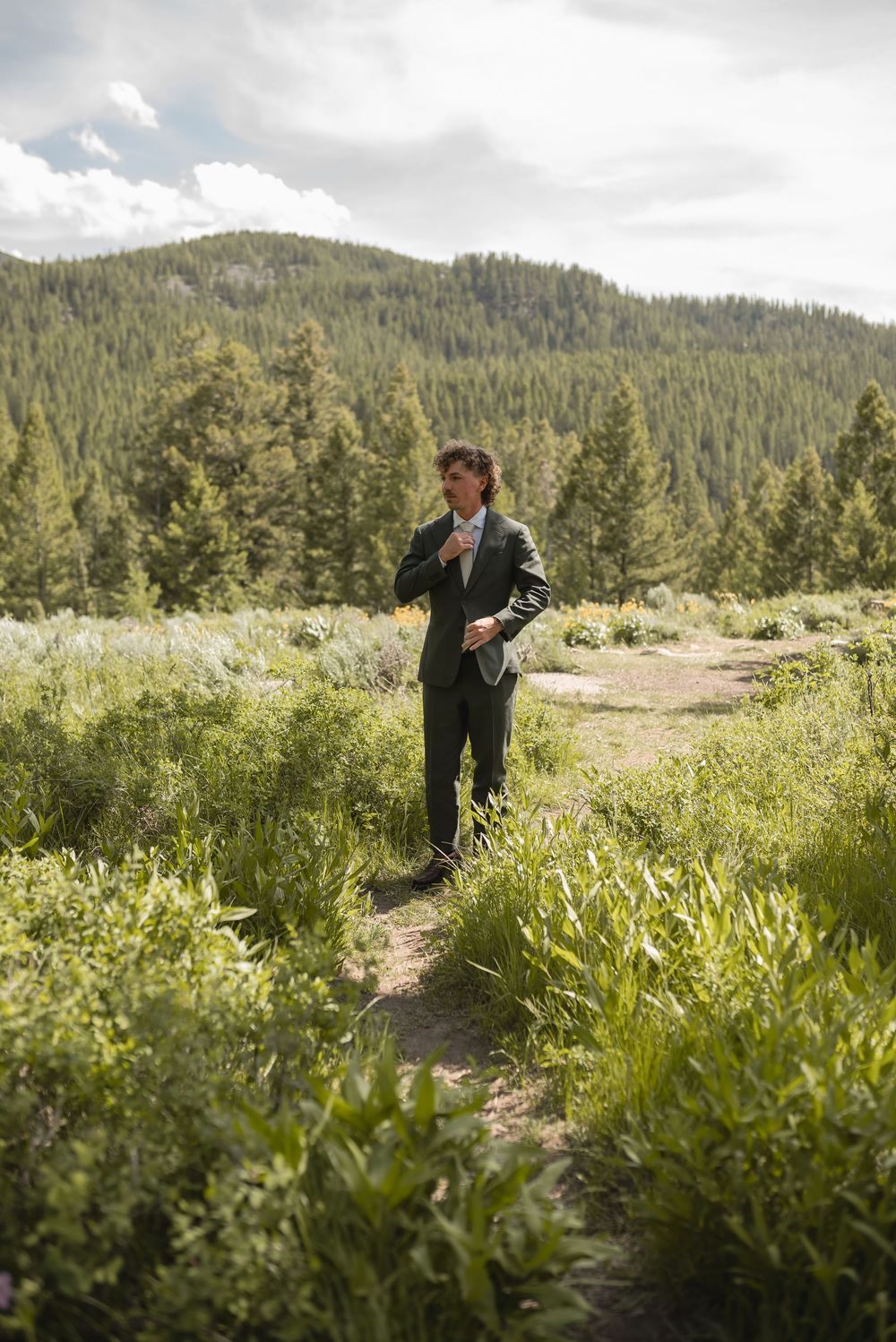 A couple shares an intimate moment on a mountain trail surrounded by lush greenery and forest views.