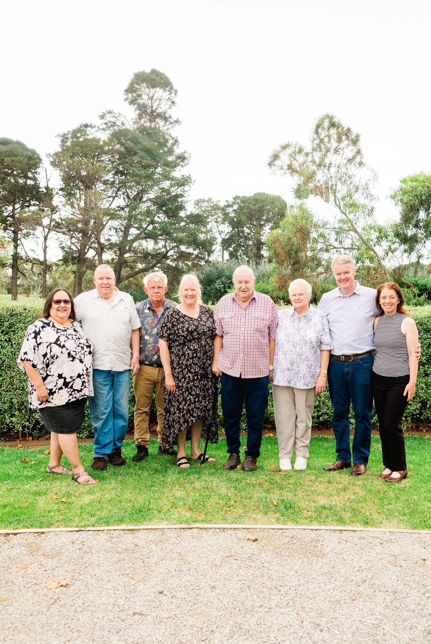 A group of people standing together outdoors on a gravel path with green trees and grass in the background.