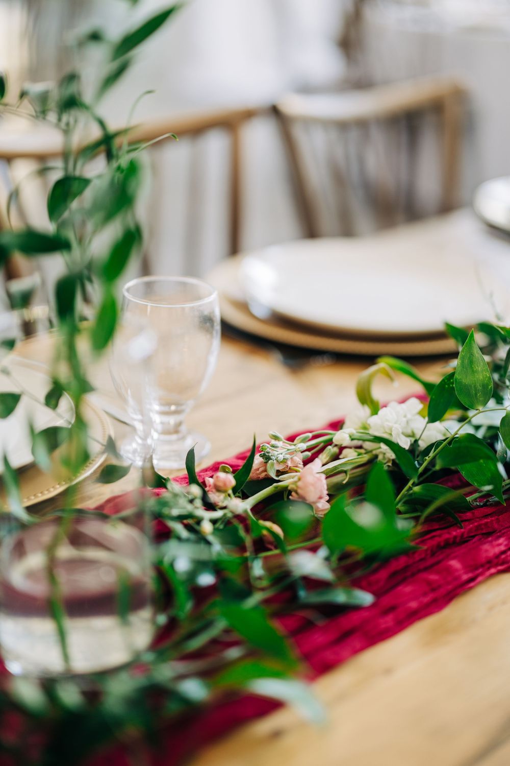 Elegant table setting with burgundy runner, greenery garland, and wine glass on wooden dining table.