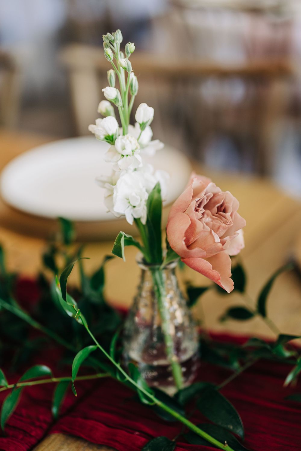 Pink carnation and white stock flowers arranged on a deep red velvet tablecloth in a glass vase.