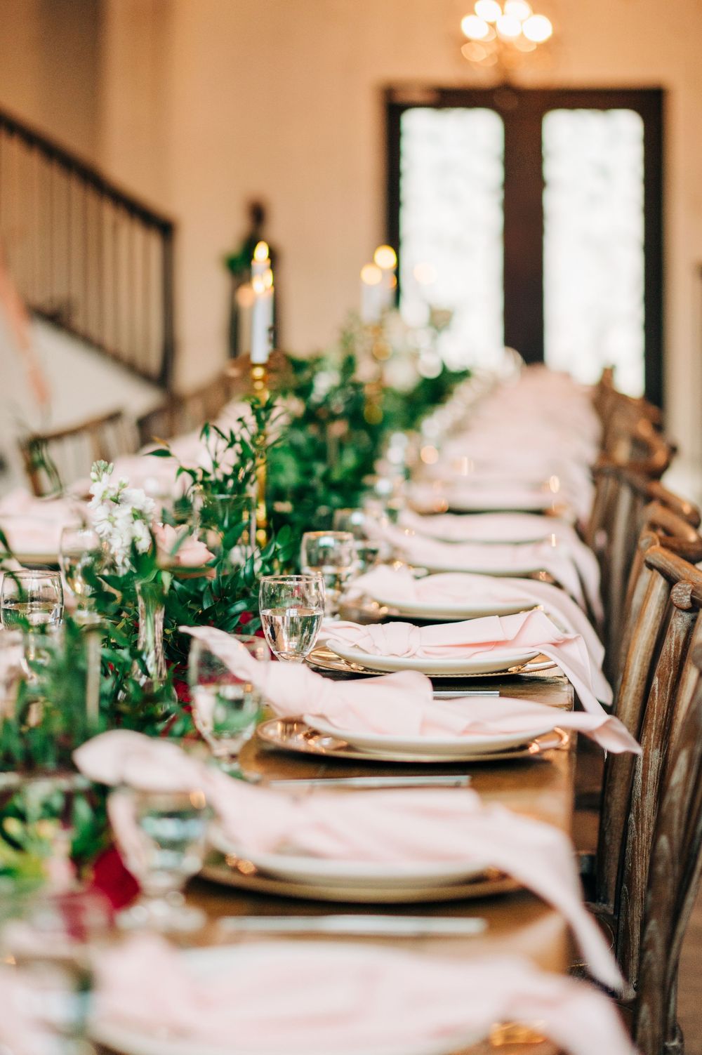 Close-up of formal table settings with white linens, place settings, and greenery garland centerpieces.
