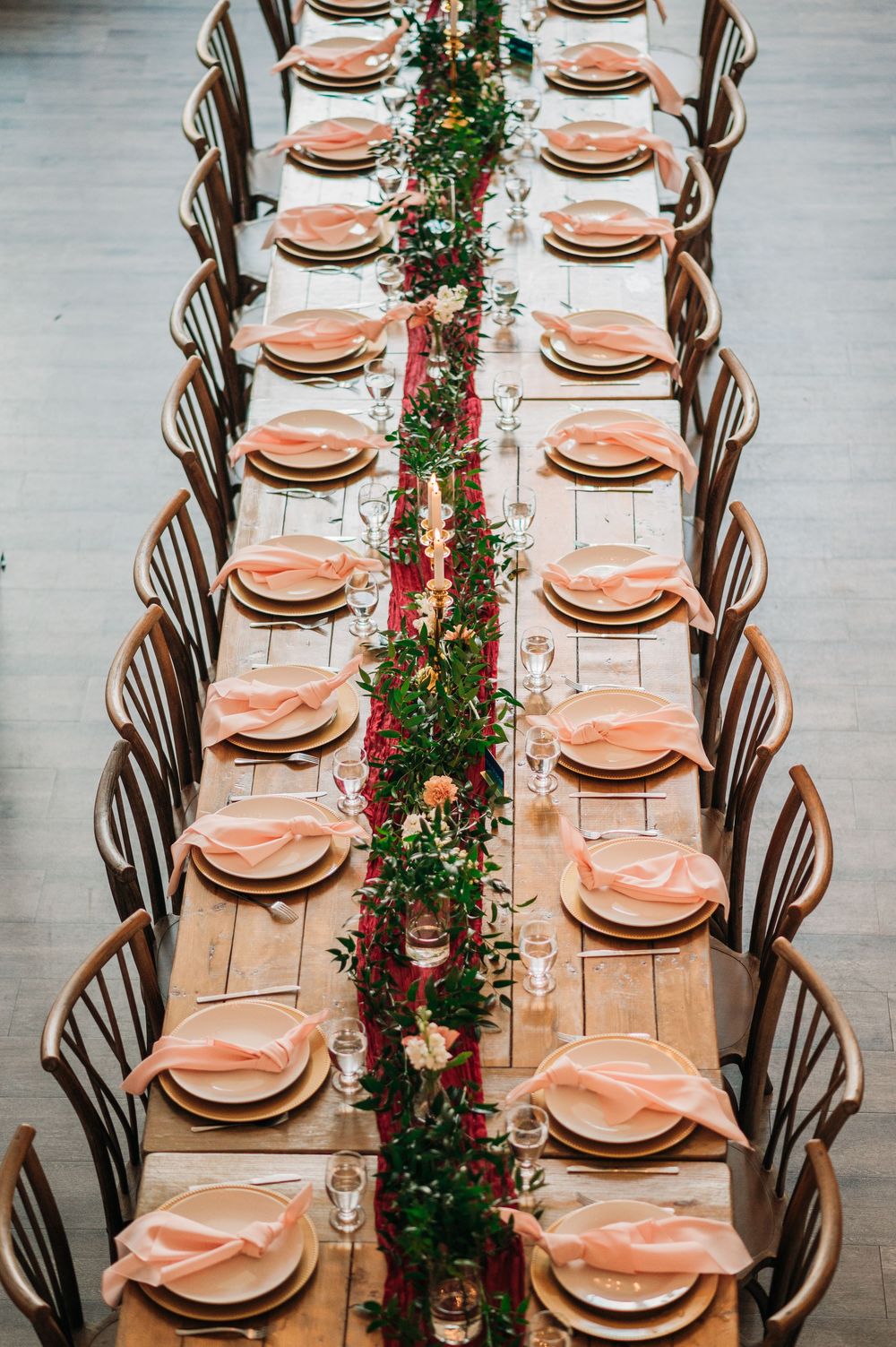 Elegant table setting with pink plates and floral garland centerpiece on rustic wooden table for wedding reception.