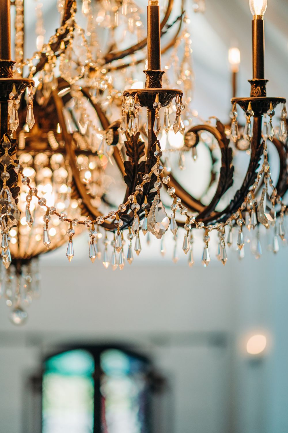Elegant crystal chandelier with hanging glass prisms casting warm golden light against a soft blue background.