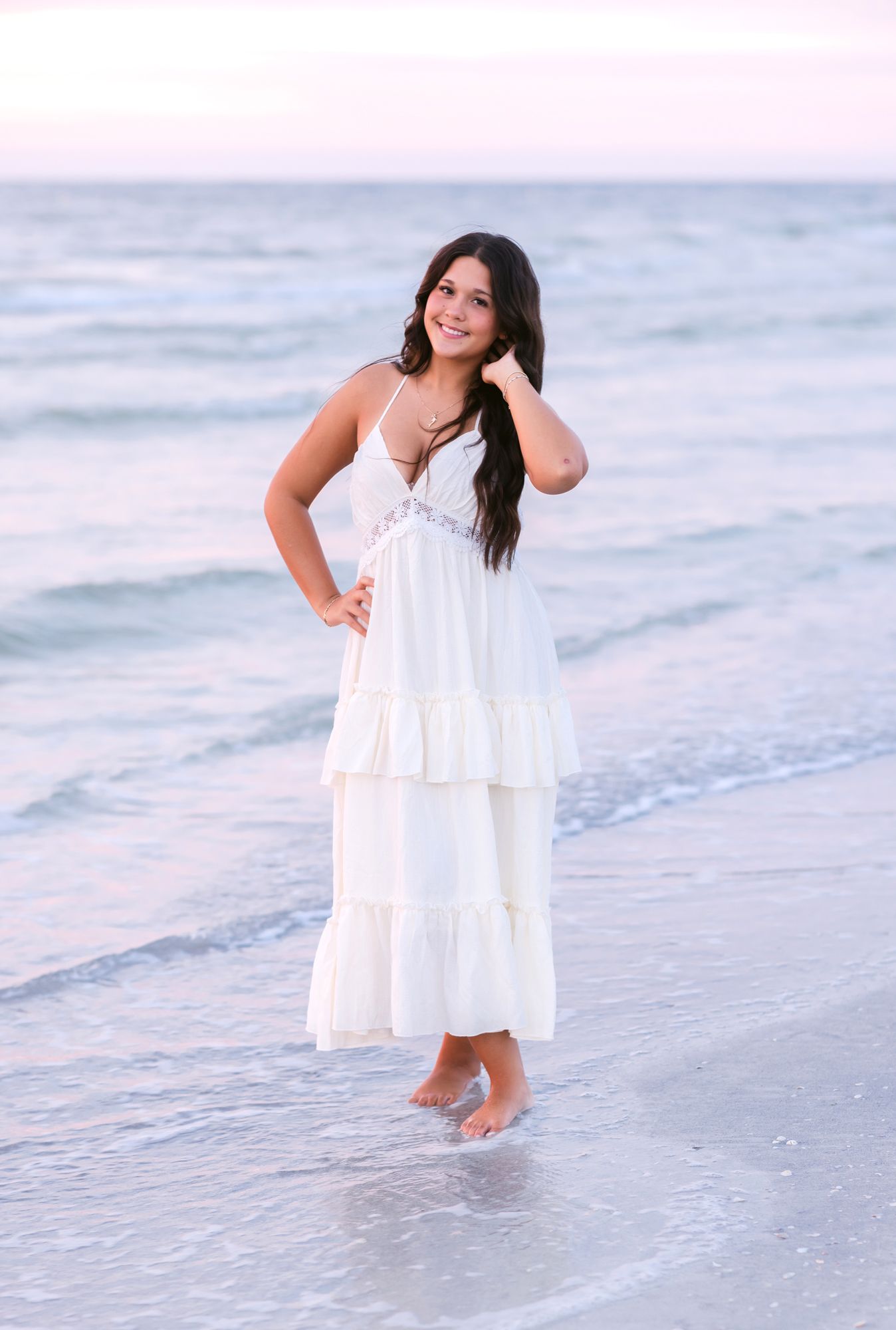 Dark, long haired girl poses standing on a beach at sunset in a white dress on Indian Rocks Beach Clearwater, Florida.