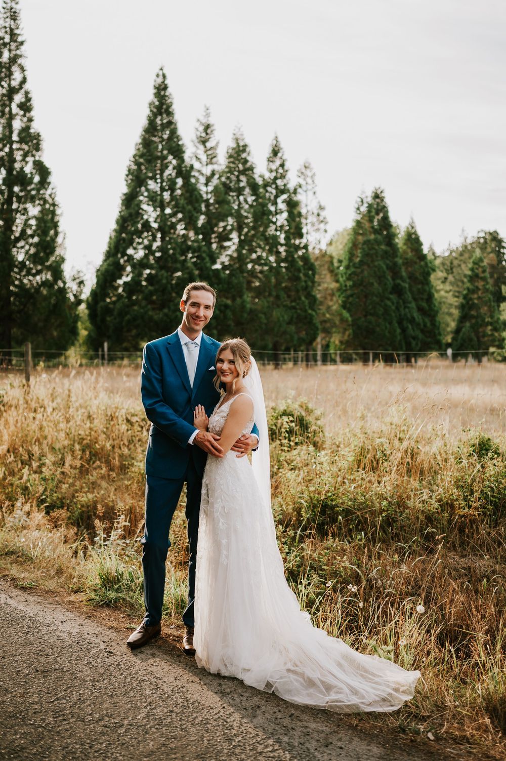 Wedding photography of couple by Williams Beach, in front of golden field in parking lot smiling at camera during golden hour