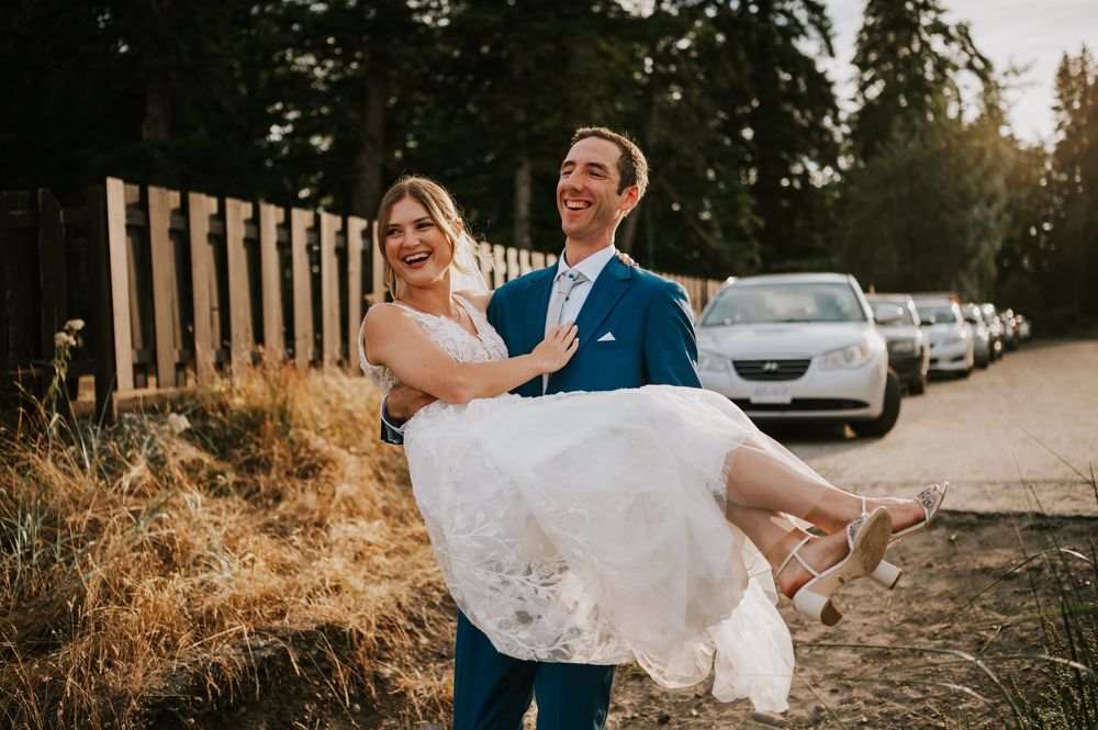 Wedding photography of couple on Williams Beach, groom carrying bride laughing during golden hour walking towards ocean