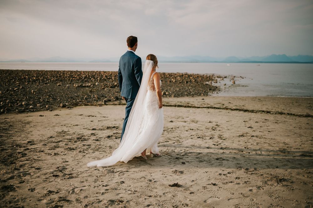 Wedding photography of couple on Williams Beach, groom walking with bride during golden hour with ocean, sand and mountains in background