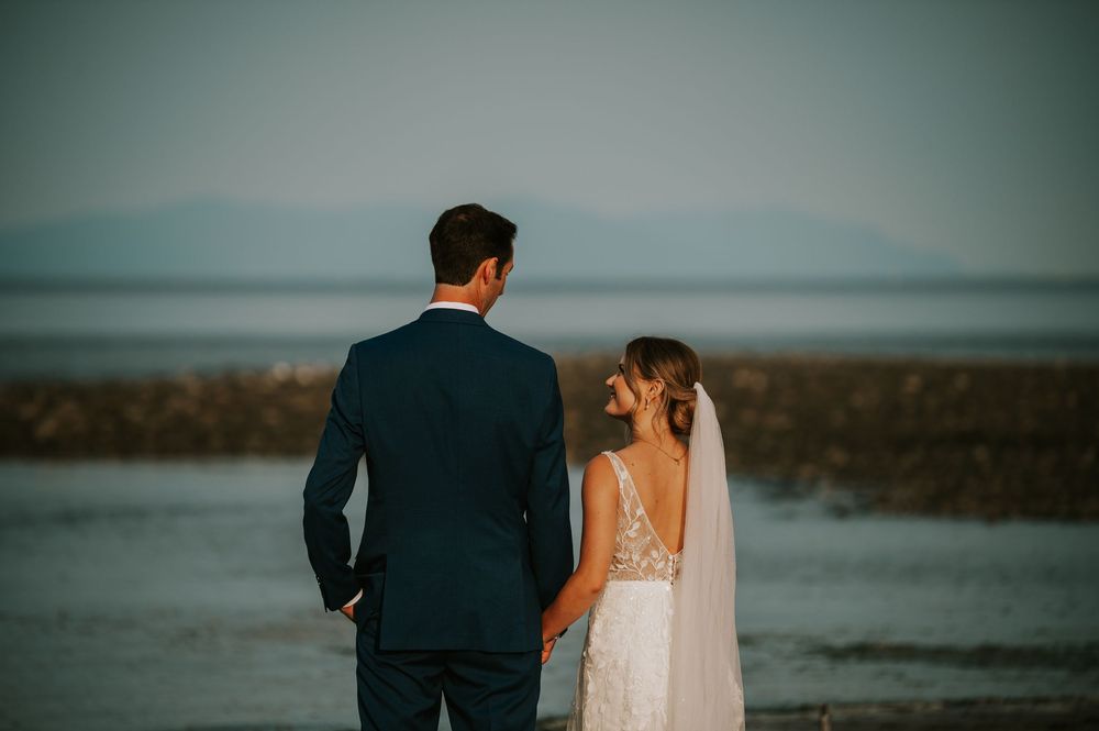 Wedding photography of couple on Williams Beach, groom looking at bride during golden hour with ocean, and mountains in background