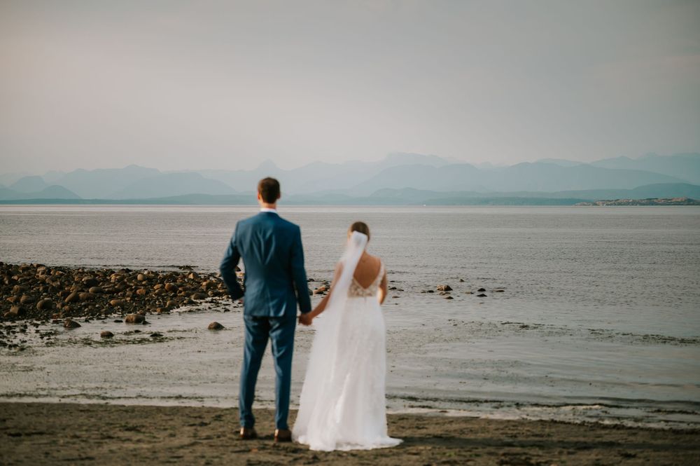 Wedding photography of couple on Williams Beach, groom and bride facing ocean during golden hour with ocean, and mountains in background