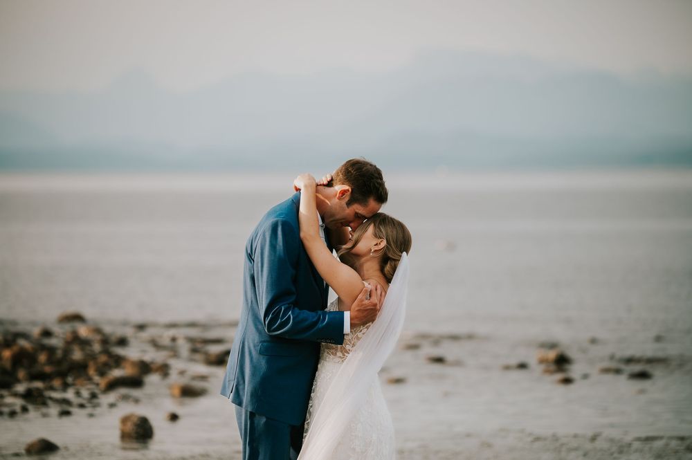 Wedding photography of couple on Williams Beach, groom and bride hugging dancing during golden hour with ocean, and mountains in background