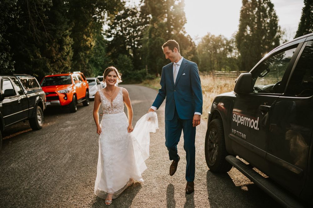 Wedding photography of couple on Williams Beach, groom carrying brides dress during golden hour walking in parking lot to ocean