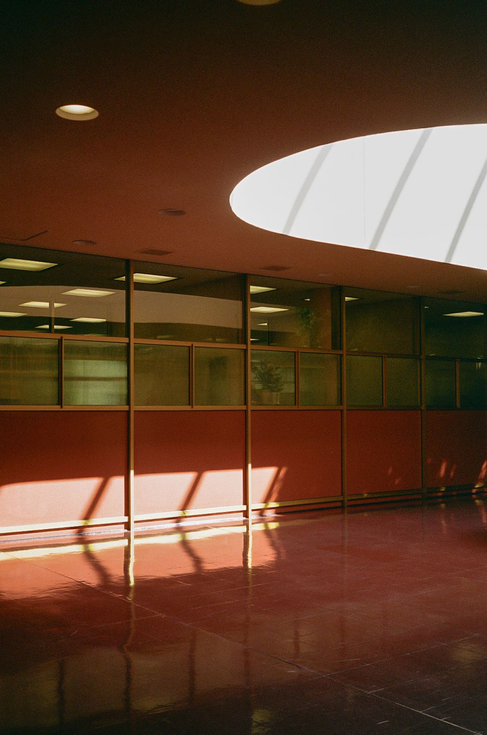 Modern interior space with circular skylight casting dramatic shadows on red floor.