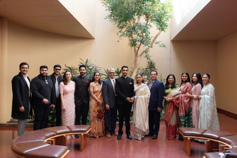 A group of elegantly dressed guests in formal Indian and Western attire pose together at an indoor venue.