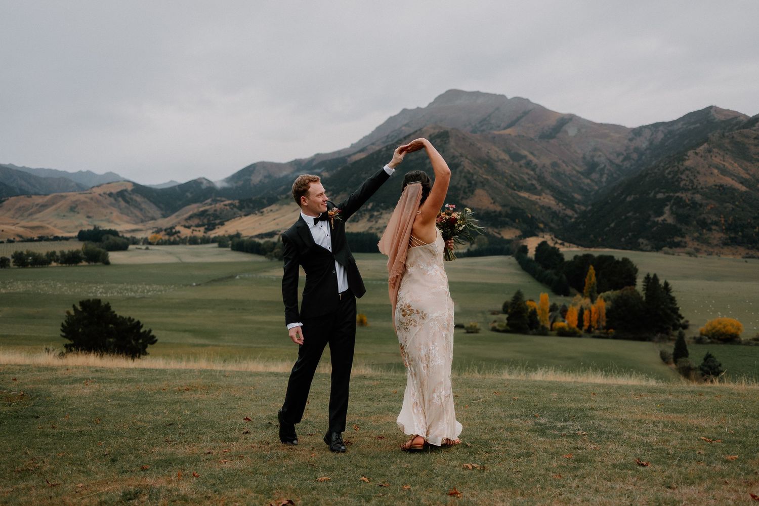 A couple dances together on a hilltop meadow with majestic mountains in the background at Lookout Lodge Wanaka, New Zealand.