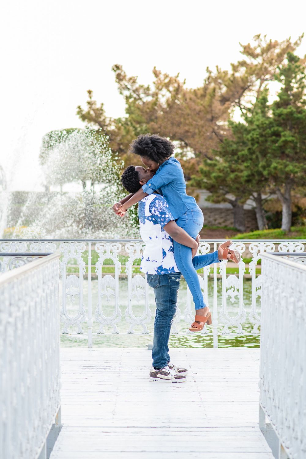 A couple shares a romantic moment on a white bridge deck with water spraying in the background.