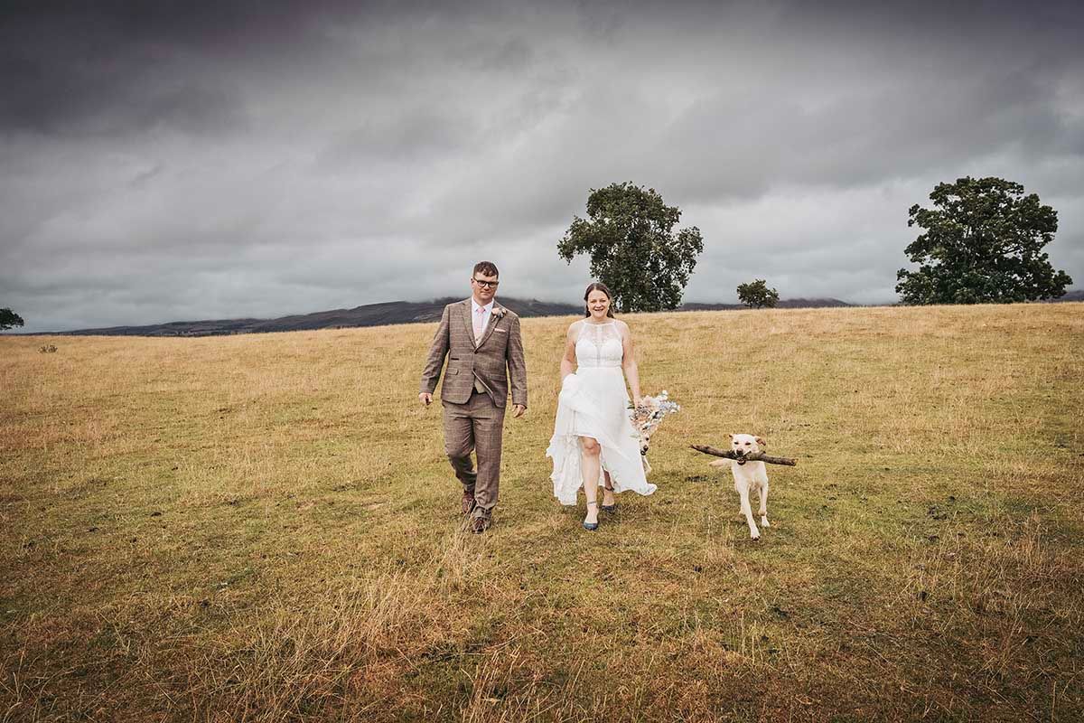 Bride in floral ball gown holding bouquet stands before a Land Rover at a stone estate at dusk.