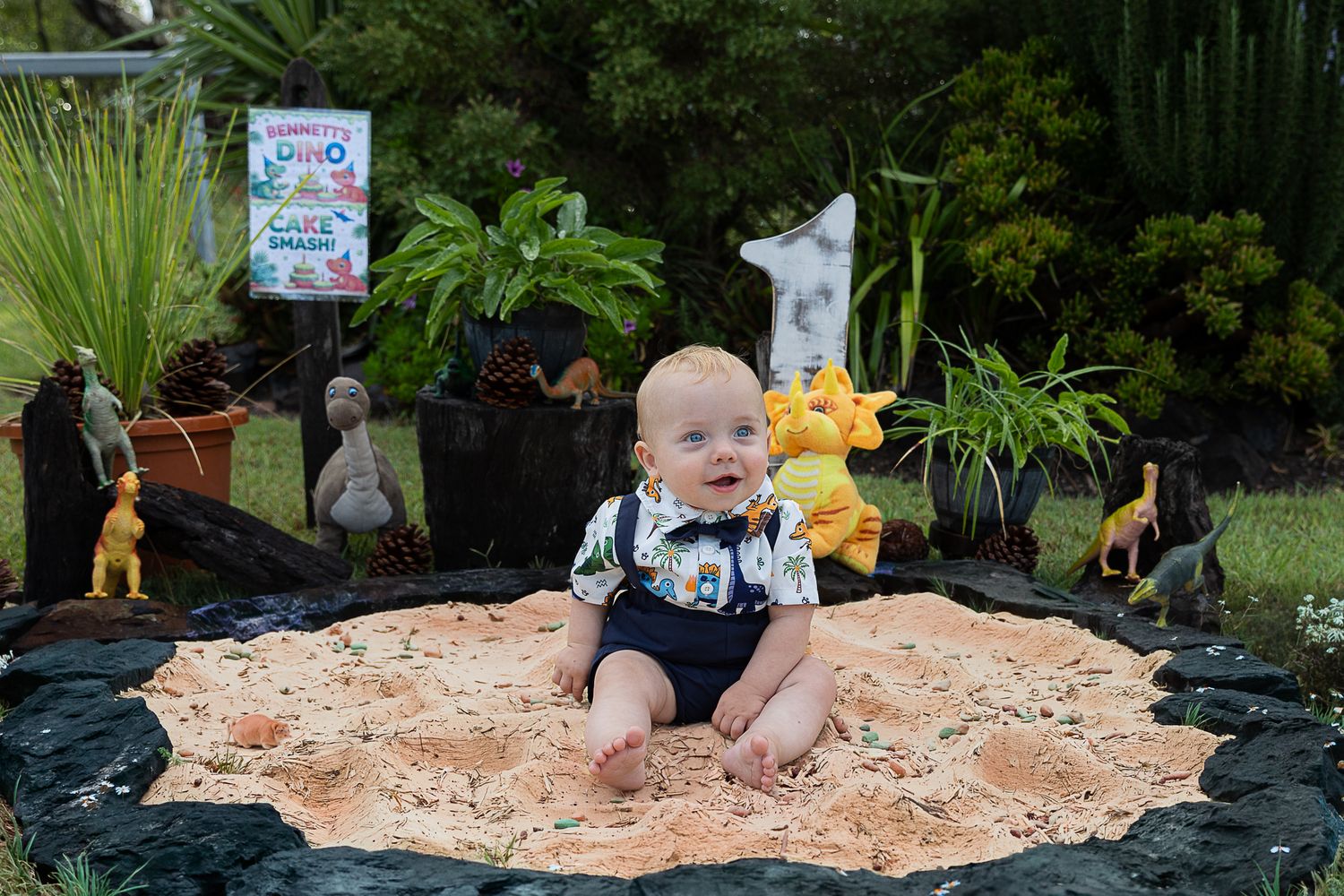 Baby boy sitting in sand at dinosaur cake smash professional photo shoot