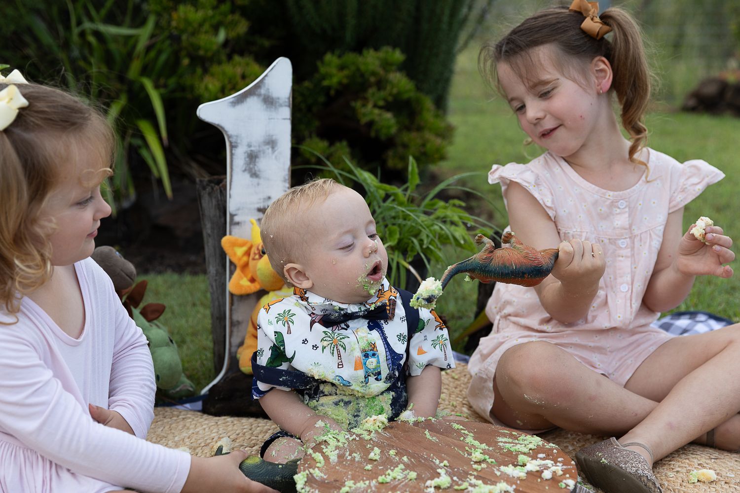 Sister feeding cake to baby brother at dinosaur cake smash professional photo shoot