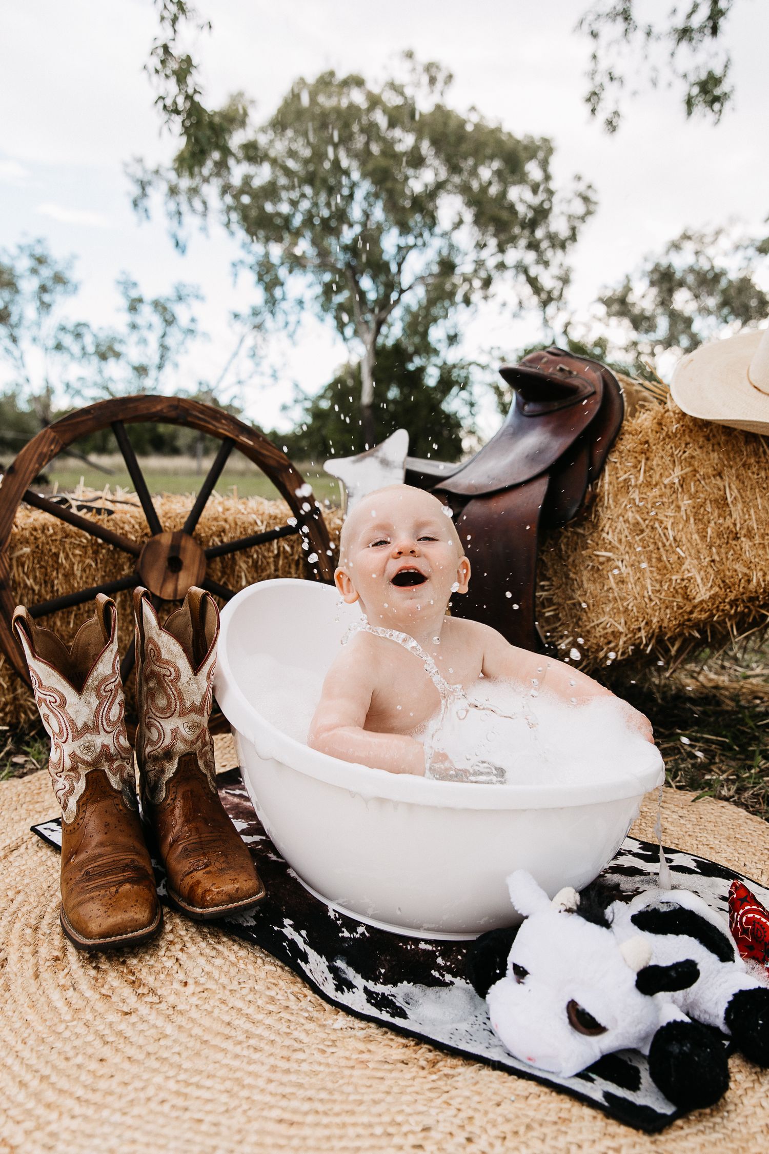 Boy splashing bubbles in a bubble bath at a cowboy cake smash photo shoot