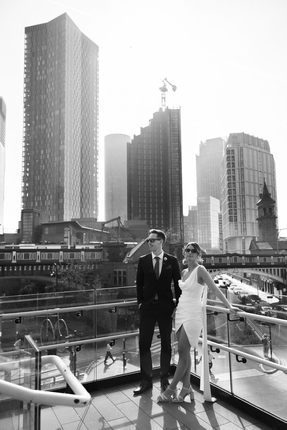 Bride and groom pose on a rooftop terrace with city skyscrapers in the background, black and white wedding photo.