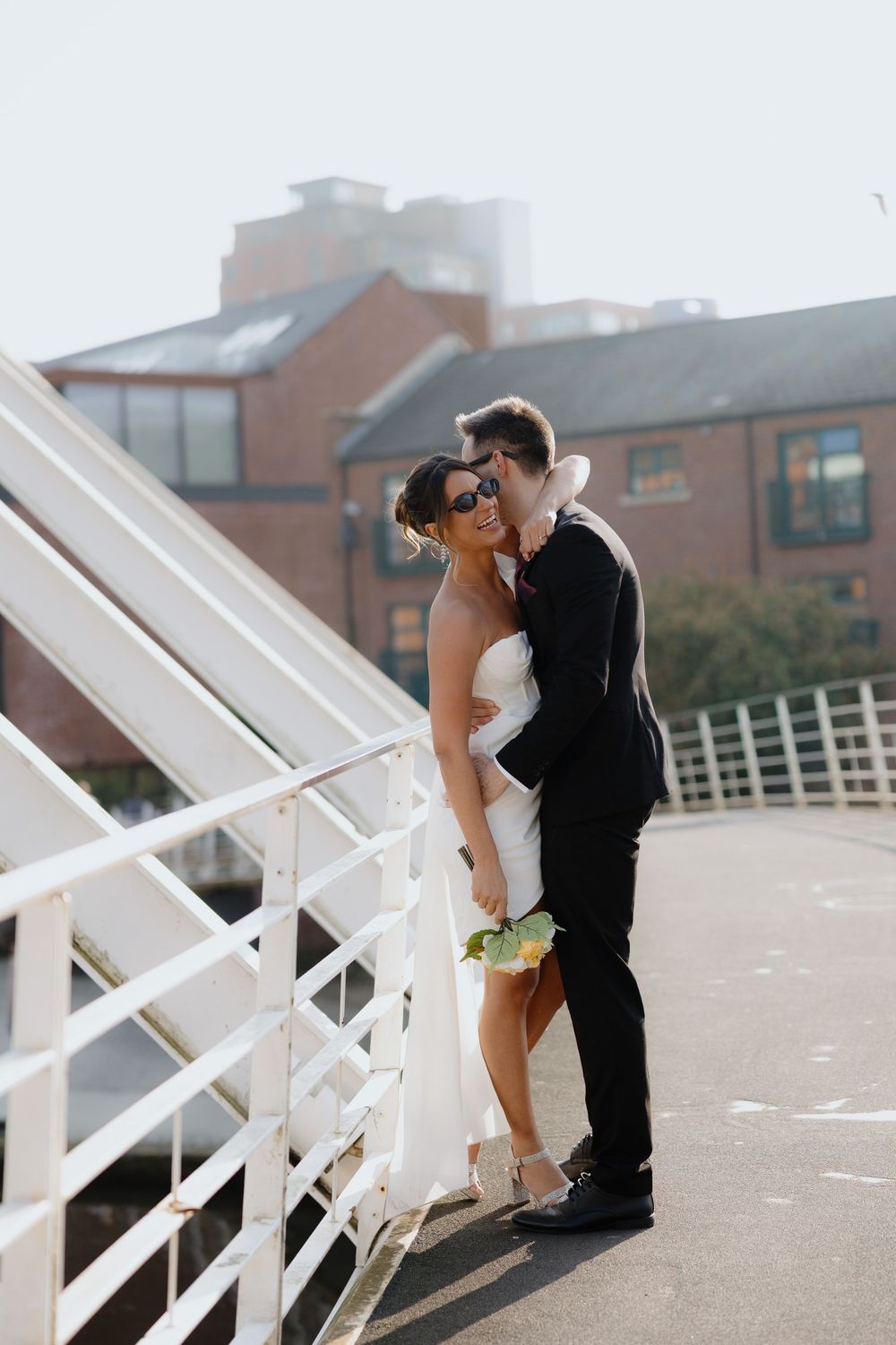 Bride and groom share a romantic kiss on a white bridge, bride wearing strapless dress holding bouquet.