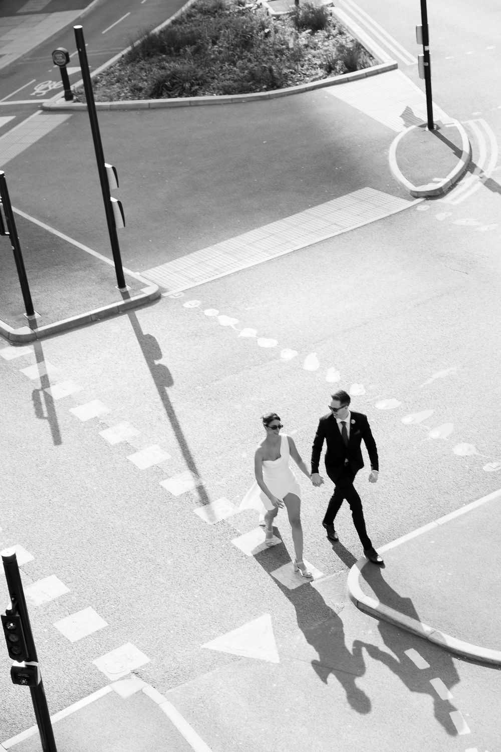 Aerial black and white photo of bride and groom walking across a city street crosswalk.