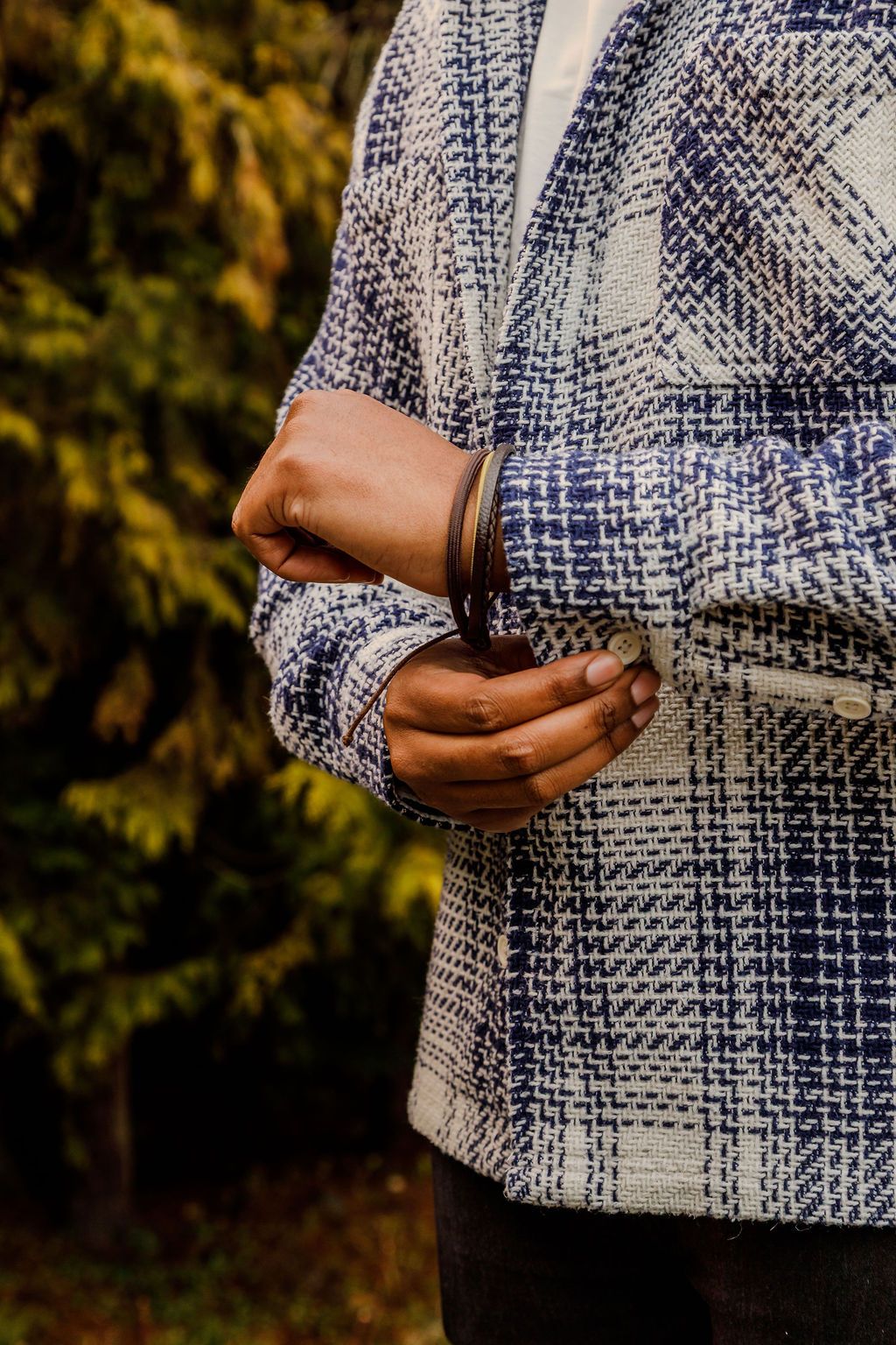 Close-up of a person adjusting the sleeve of a blue and white plaid tweed blazer outdoors.