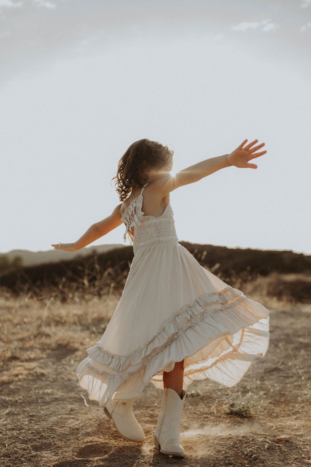 A figure in a flowing white dress twirls and dances in a golden field at sunset.