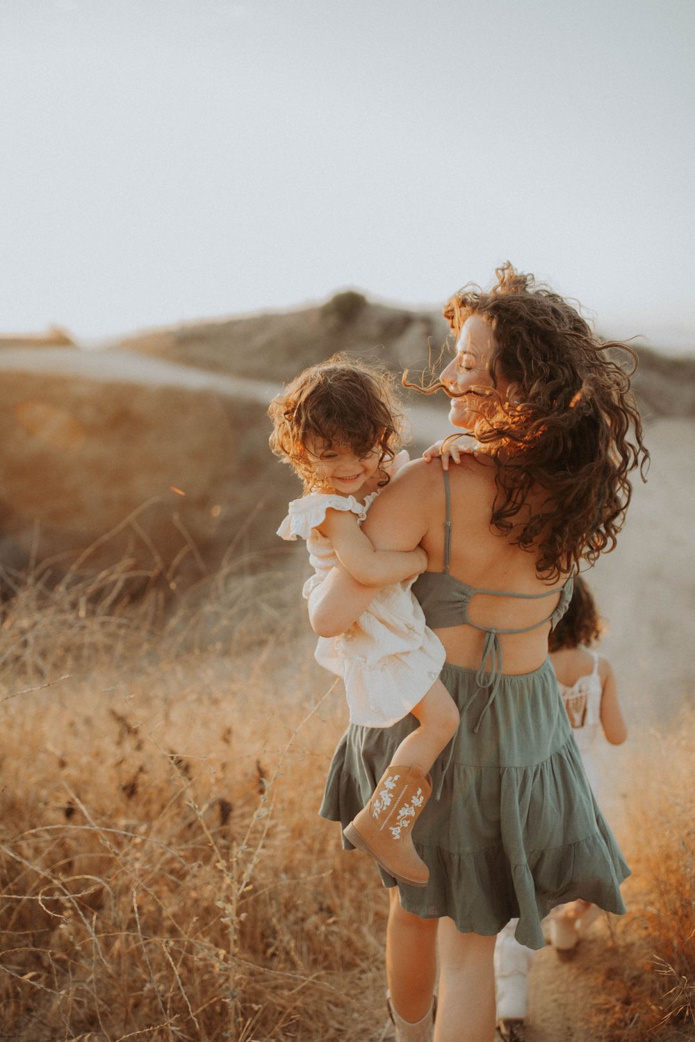 A tender moment captured at sunset in a golden field with flowing dresses and curly hair caught in the warm breeze.