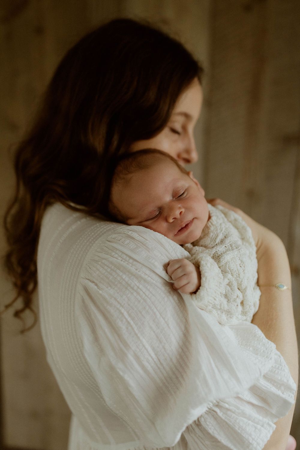 A tender moment captured as a sleeping newborn baby rests peacefully against a shoulder in a white sweater.