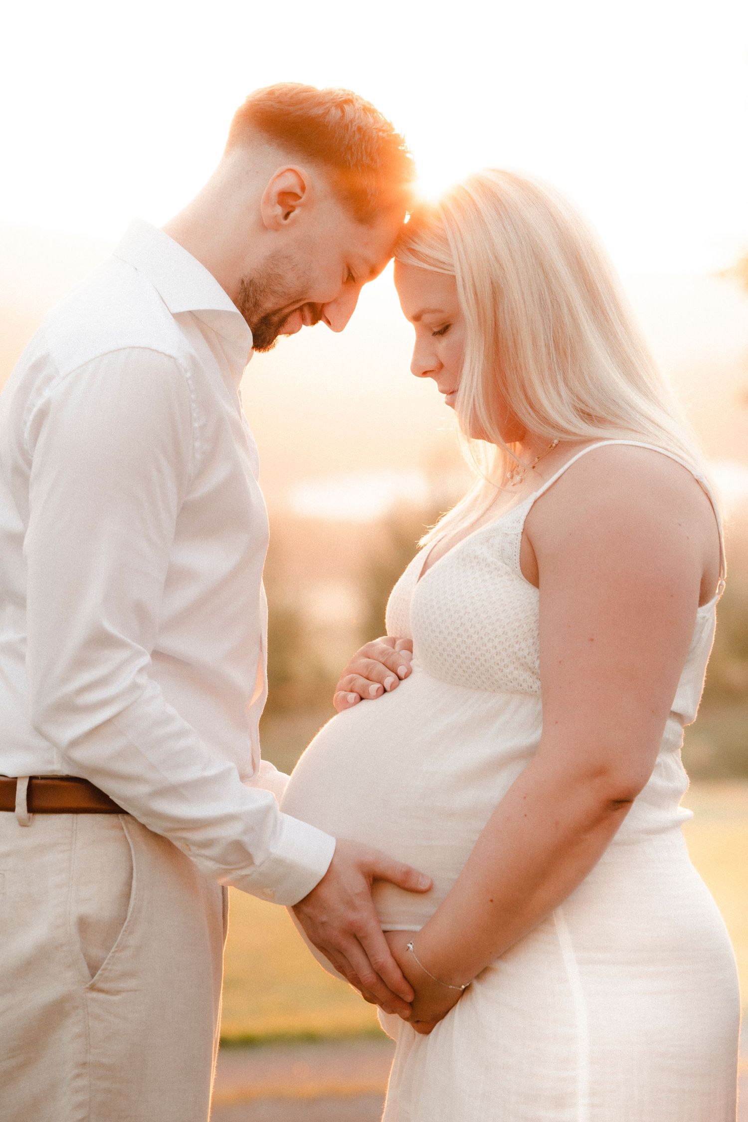 Romantic maternity photo series showing couple in white clothing embracing during sunset with warm golden lighting.