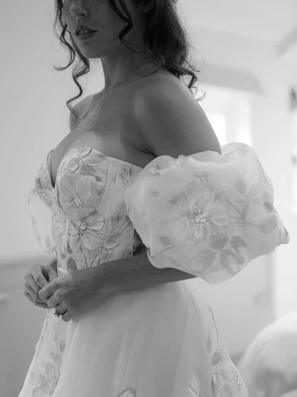 Close-up black and white photo of bride in off-shoulder floral wedding gown with voluminous organza puff sleeves.