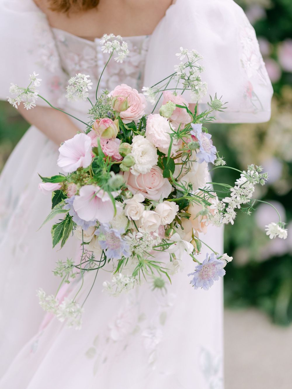 Bride holding a lush cascading wedding bouquet with pink roses, sweet peas, and wildflowers in soft pastel hues.