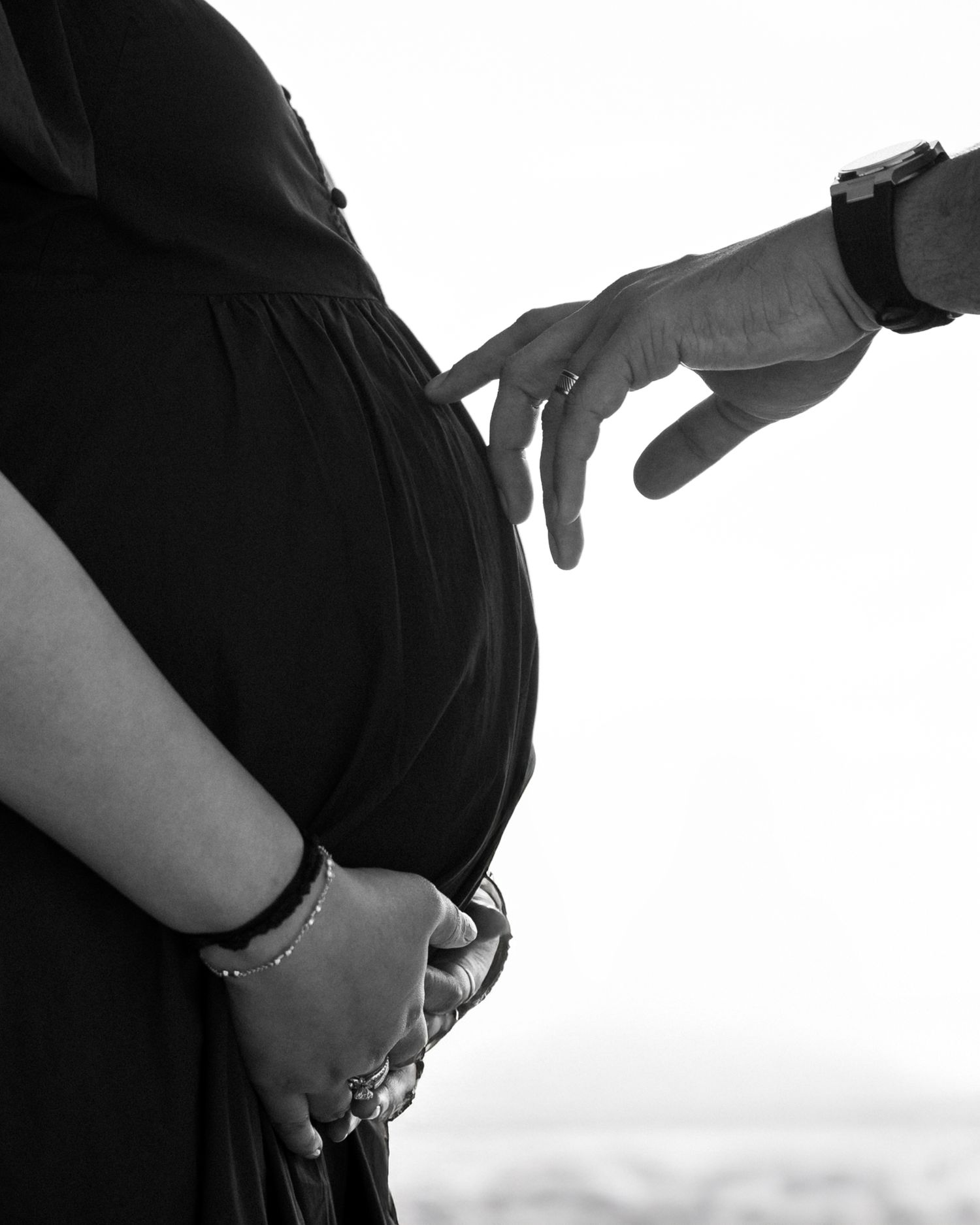 Black and white maternity photoshoot close-up of baby bump with partner’s hand