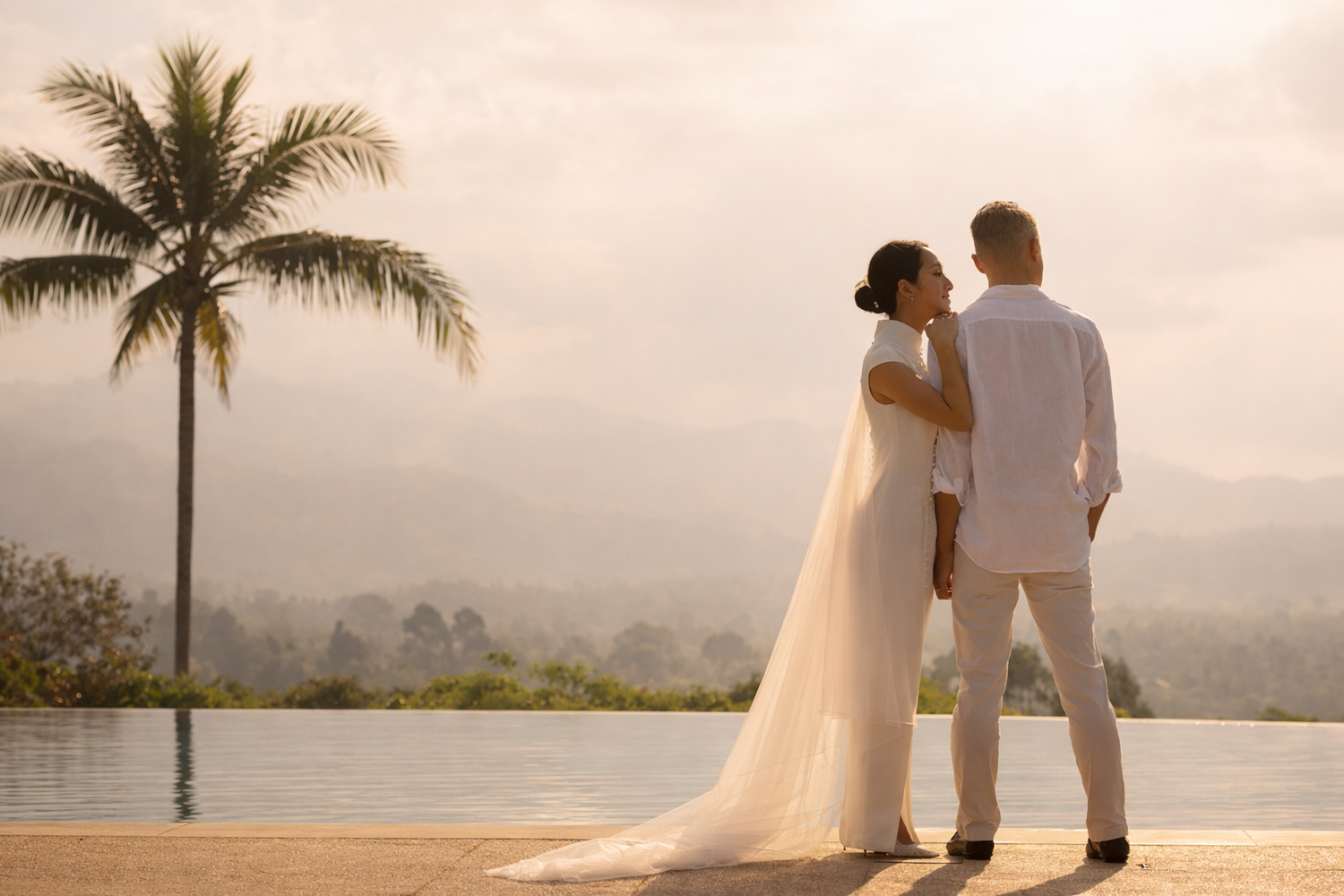 Elegant couple by infinity pool at sunrise in Koh Samui, overlooking tropical hills and palm tree—refined, cinematic pre-wedding moment