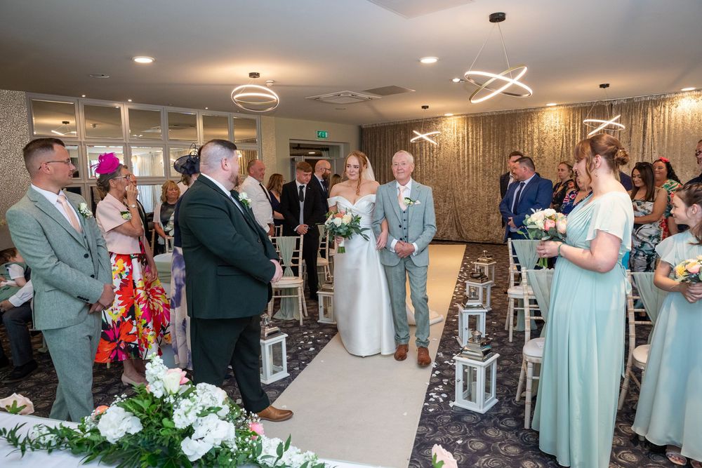 Bride walks down the aisle with her father at an elegant indoor wedding ceremony.