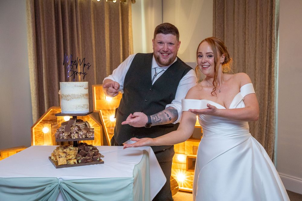 Smiling bride and groom cut their elegant white wedding cake together at their reception.