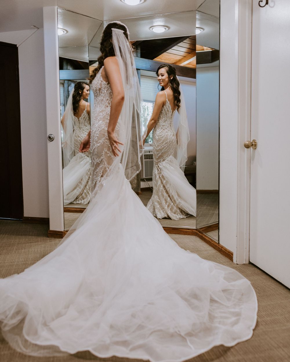 Bride in lace mermaid gown with cathedral veil reflected in dressing room mirrors.