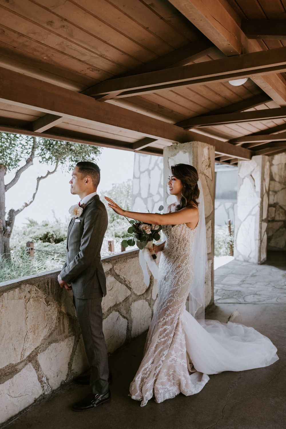 Bride surprises groom during first look on rustic stone terrace at wedding venue.