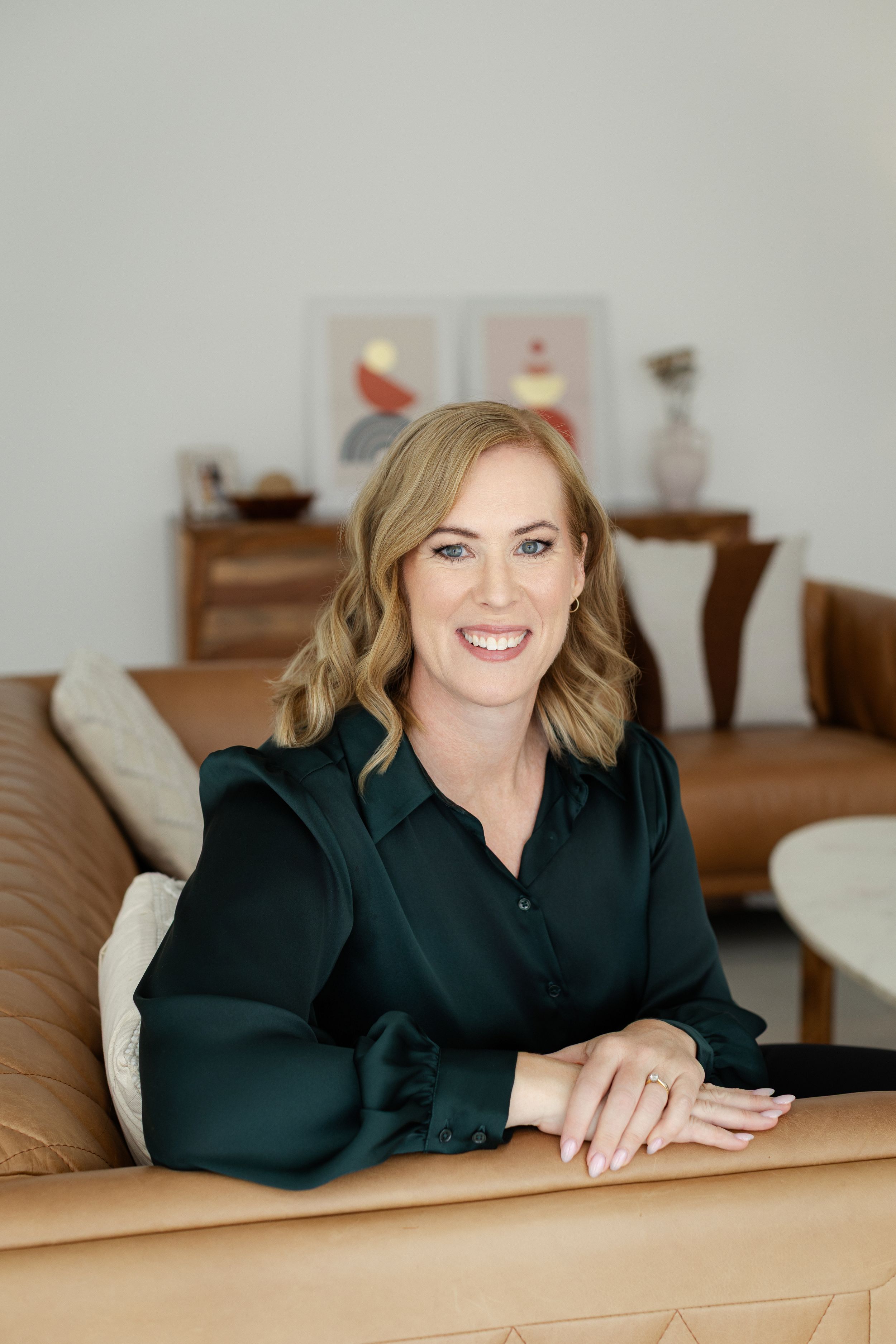 Professional headshots showing someone in a black top reclining on a brown couch in an interior setting.