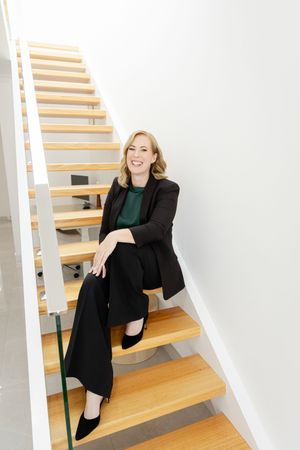 Modern interior photoshoot featuring someone posing on wooden stairs against white walls.