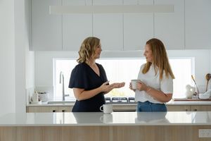Two people talking in a bright white kitchen over coffee
