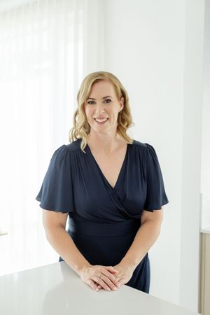 Business professional in navy dress smiling warmly in front of white backdrop during photo session.