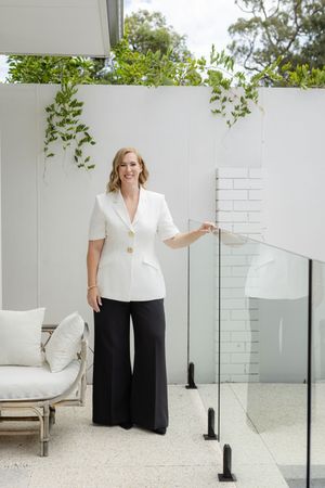 Professional portrait series in white outfit against modern white wall with glass railing and greenery.