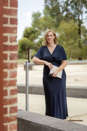 A person in a navy blue dress poses in different positions against a brick wall and railing outdoors.